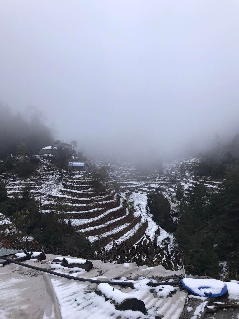 The image feels dark and cold with sky obscured by low grey cloud. Terraced hills appear to be striped by the bands of snow on level ground.