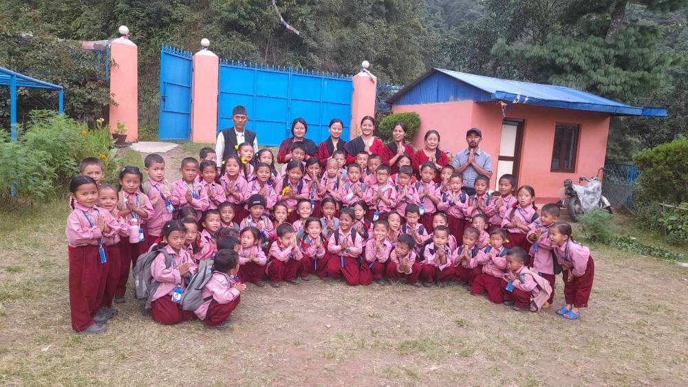 The whole school are posed with children at the front and staff behind, dressed in uniforms of burgundy, pink and black.