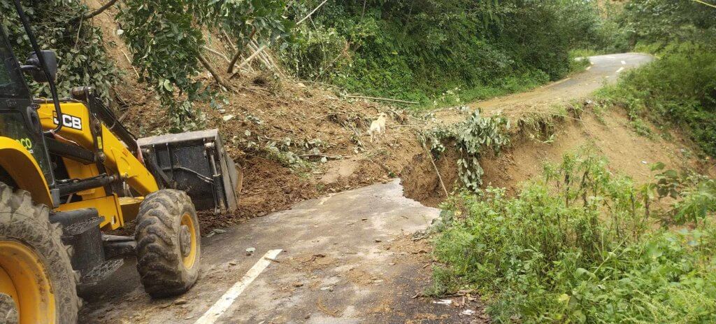 A digger approaches the landslide that is blocking the road to the school. Beyond the landslide half the width of the road has collapsed.