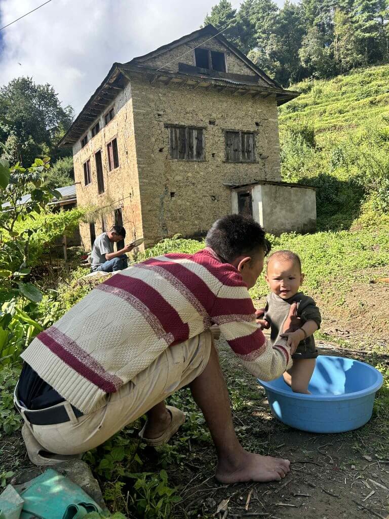 A man baths a baby in the fresh air beside a two story home with a windowed loft.
