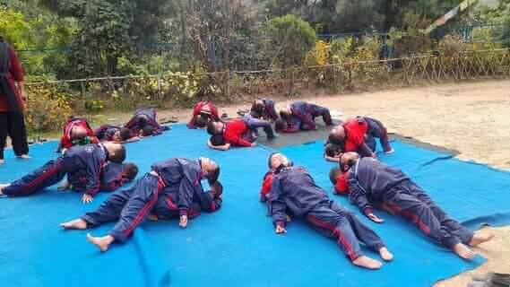 A mixed age group are working in pairs - one in child’s pose with forehead on the ground, the partner lying back to back and looking up.